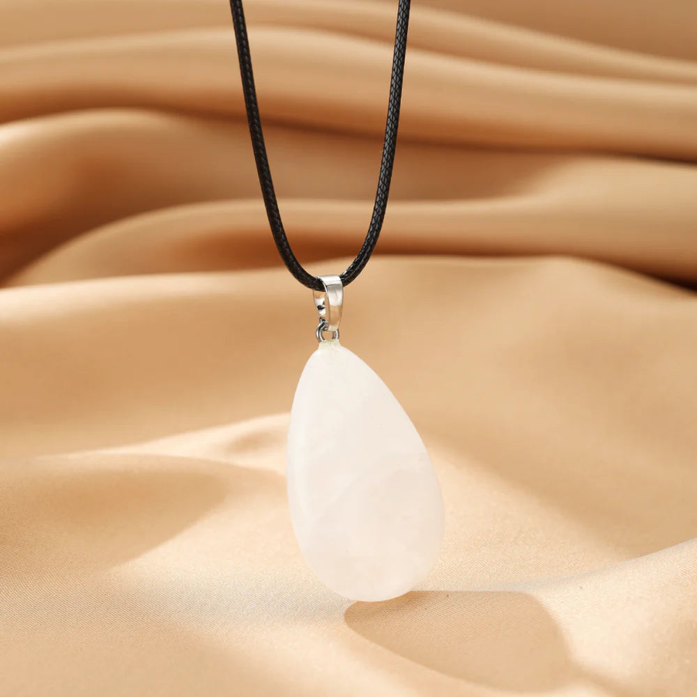 Collier "Lumière Pure" avec pendentif en forme de goutte en cristal de roche blanc laiteux sur un fond satiné beige.