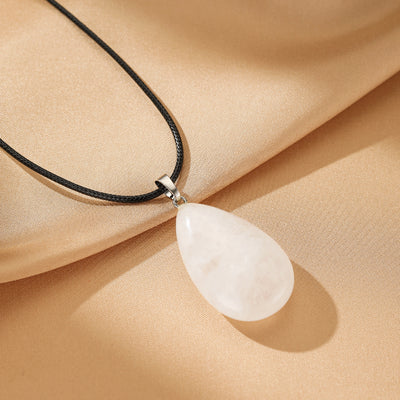 Collier pendentif en forme de goutte en cristal de roche blanc translucide sur un cordon noir.