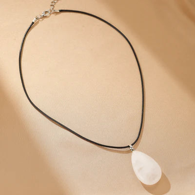 Collier avec pendentif en forme de goutte en cristal de roche blanc sur un cordon noir.
