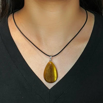 Collier "Goutte Protectrice" avec un pendentif en œil de tigre en forme de goutte, porté autour du cou d'une personne portant un haut noir.