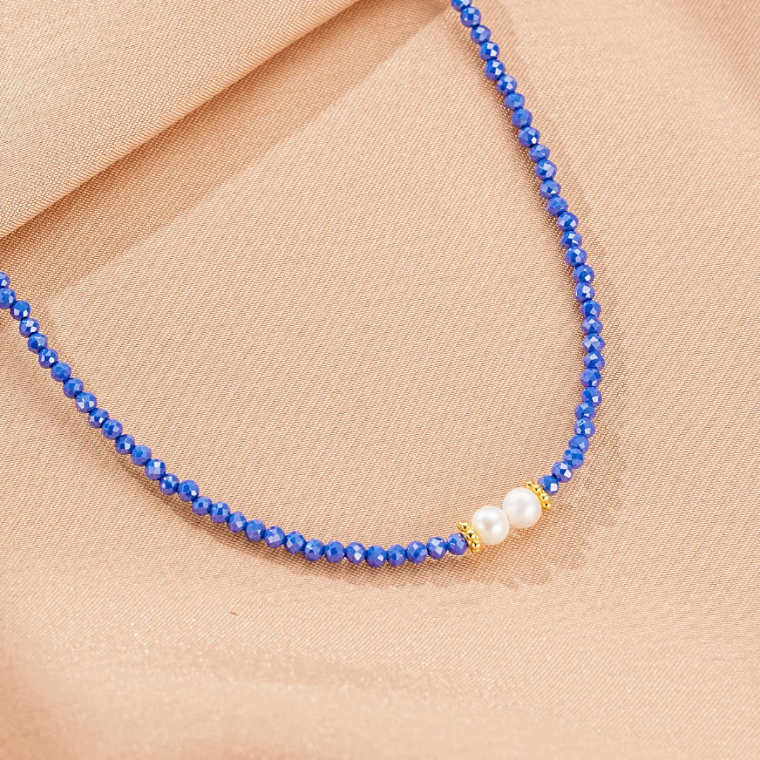Collier "Délicatesse" fait de petites perles bleues en lapis lazuli et deux perles blanches nacrées, avec de petites perles dorées entre chaque perle.
