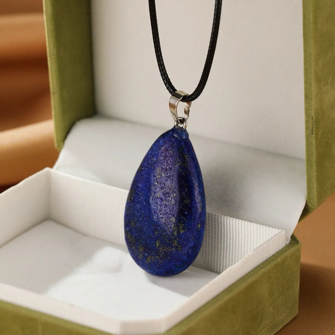 Collier "Goutte de Sagesse" avec un pendentif en forme de goutte de lapis-lazuli bleu profond, monté sur un cordon noir et présenté dans une boîte cadeau verte.
