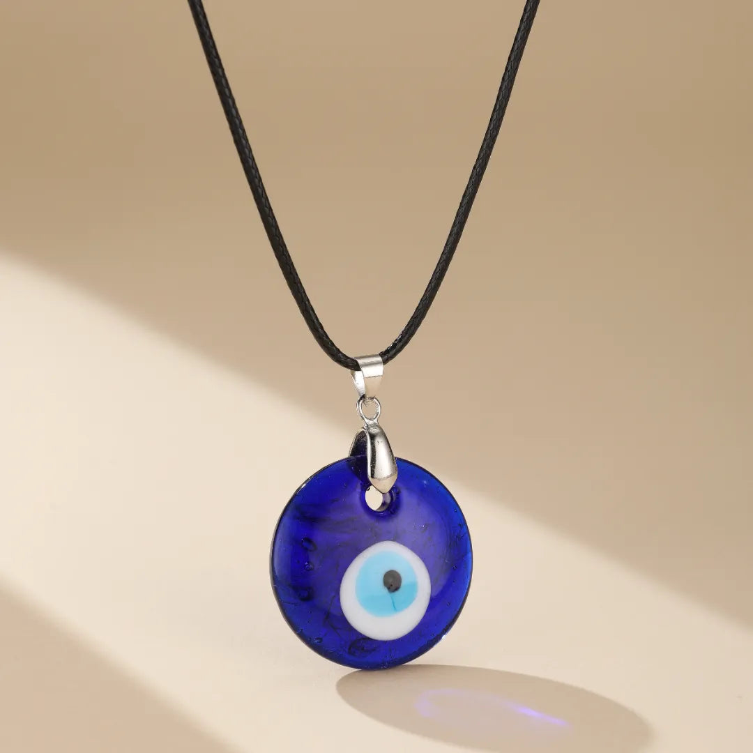 Collier avec un pendentif rond bleu foncé représentant un œil bleu, suspendu à un cordon noir.