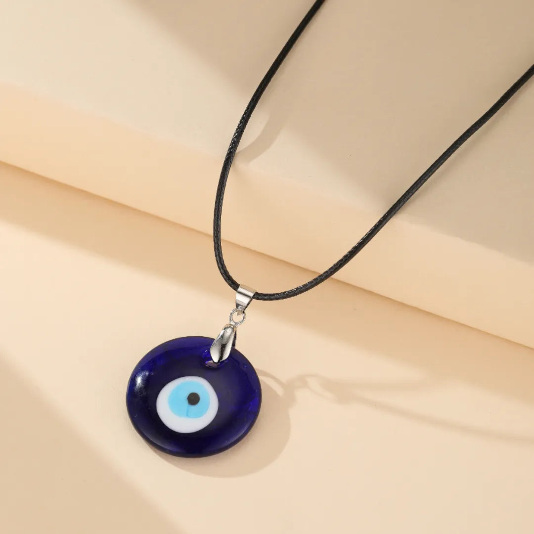Collier Mauvais Œil "Œil Bleu" avec un pendentif rond bleu foncé orné d'un œil stylisé blanc et bleu clair, suspendu à un cordon noir.