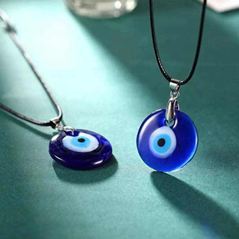 Deux colliers avec un pendentif œil bleu de protection sur un fond vert sarcelle.