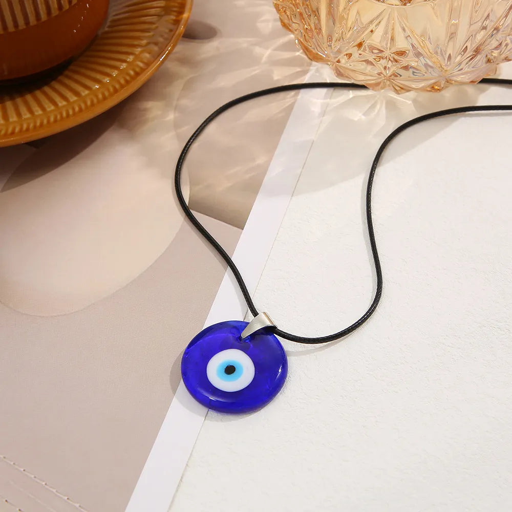 Collier de protection "Œil Bleu" avec un pendentif rond en verre bleu vif orné d'un motif d'œil stylisé aux cercles concentriques bleu et blanc, suspendu à un cordon noir.