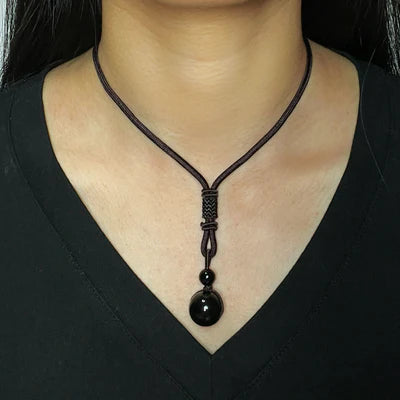 Collier ras du cou avec une boule d'obsidienne noire polie et une plus petite perle d'obsidienne suspendue à un cordon tressé réglable.
