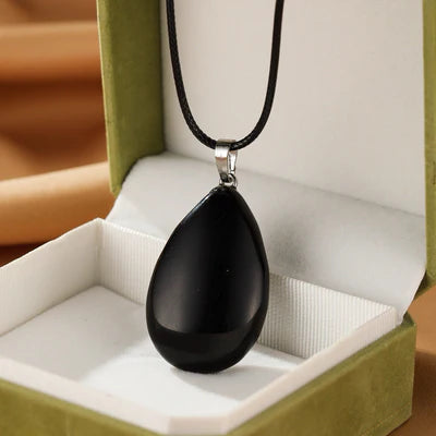 Collier avec pendentif en forme de goutte d'obsidienne noire polie, monté sur un cordon noir, présenté dans une boîte cadeau verte.