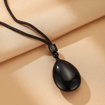 Collier avec pendentif en forme de larme en obsidienne noire polie, suspendu à un cordon noir avec une perle et un fermoir décoratif en forme de nuage.