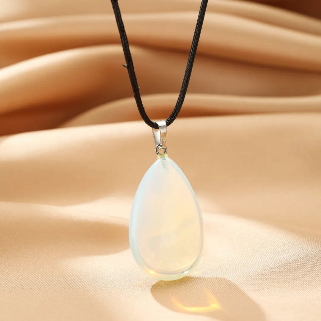 Collier avec un pendentif opale en forme de larme blanche et nacrée, suspendu à un cordon noir.