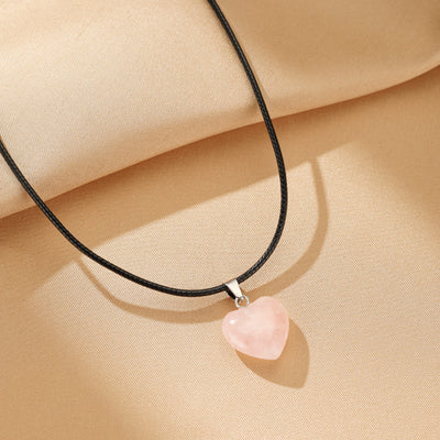 Collier avec pendentif en forme de cœur en quartz rose sur un fond beige texturé.