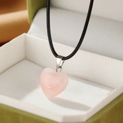 Collier pendentif en forme de cœur en quartz rose, avec un cordon noir, présenté dans une boîte cadeau.