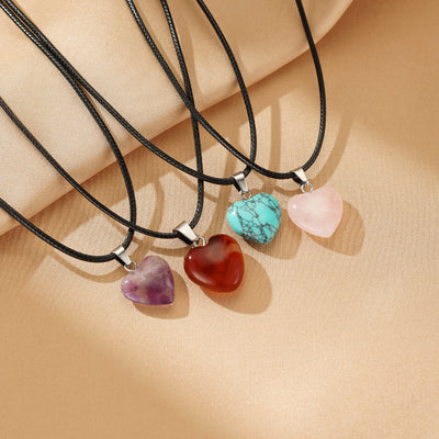 Collier en quartz rose en forme de cœur apaisant, avec d'autres pendentifs en pierre naturelle de différentes couleurs sur des cordons noirs.