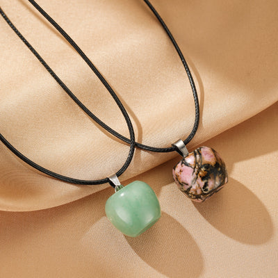 Deux colliers avec des pendentifs en pierre naturelle carrés, l'un vert et l'autre rose veiné de noir, sur des cordons noirs.