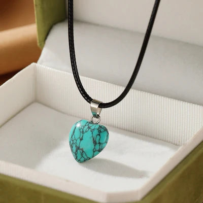 Collier avec pendentif en forme de cœur en turquoise brute sur un cordon noir, présenté dans une boîte cadeau verte.