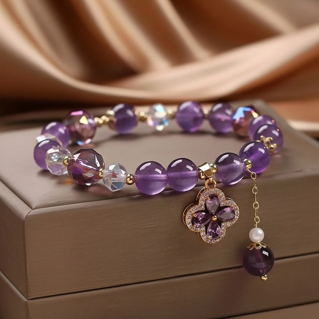 Bracelet en améthyste avec pendentif trèfle à quatre feuilles incrusté de cristaux et une perle, sur un fond de soie dorée
