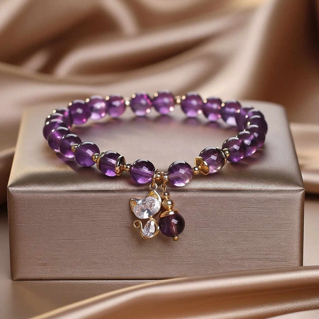 Bracelet fait de perles d'améthyste et de petits éléments dorés, orné d'un pendentif en forme de chat incrusté de strass et d'une petite perle d'améthyste.